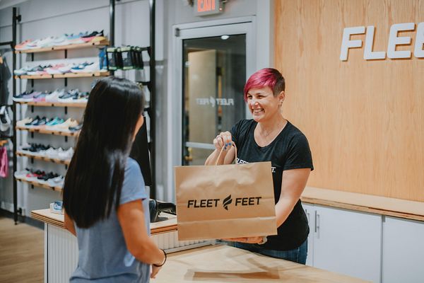A Fleet Feet outfitter hands a customer their purchase.