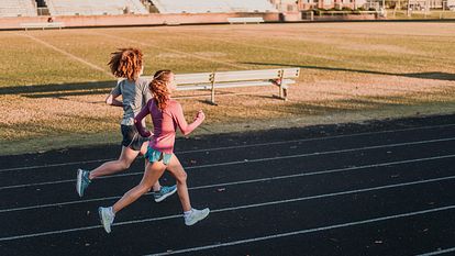 Two girls run around an outdoor track.